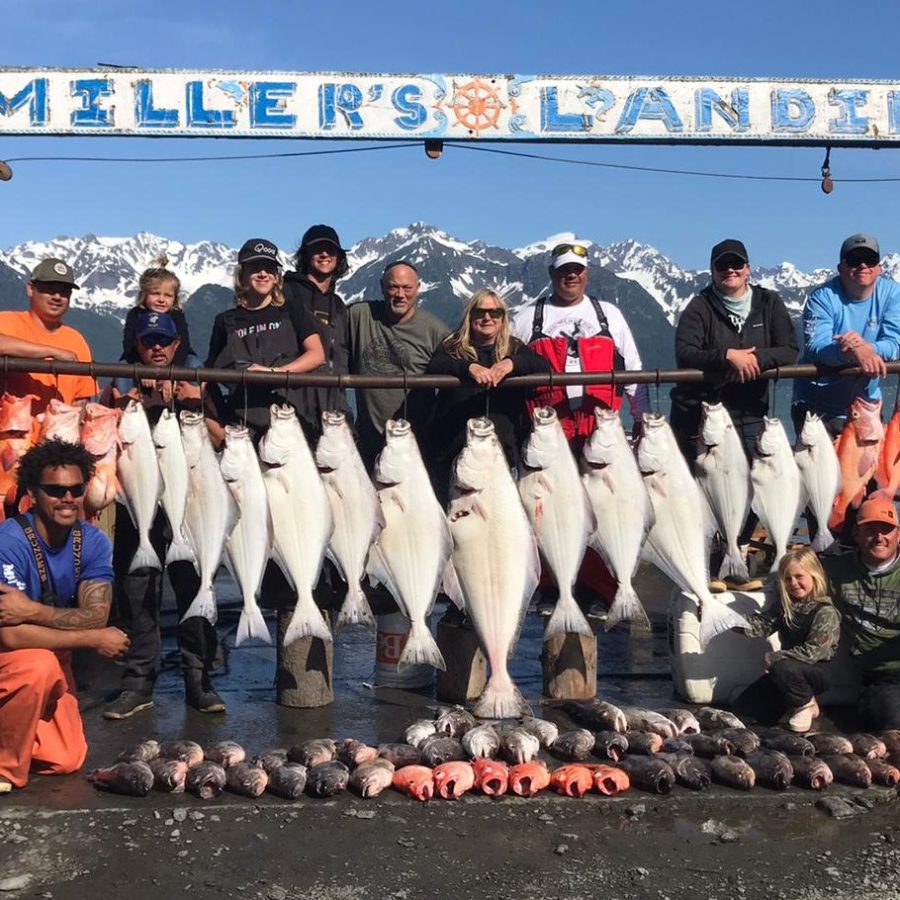 Group posing with large fish catch at Miller's Landing, snowy mountains in background.