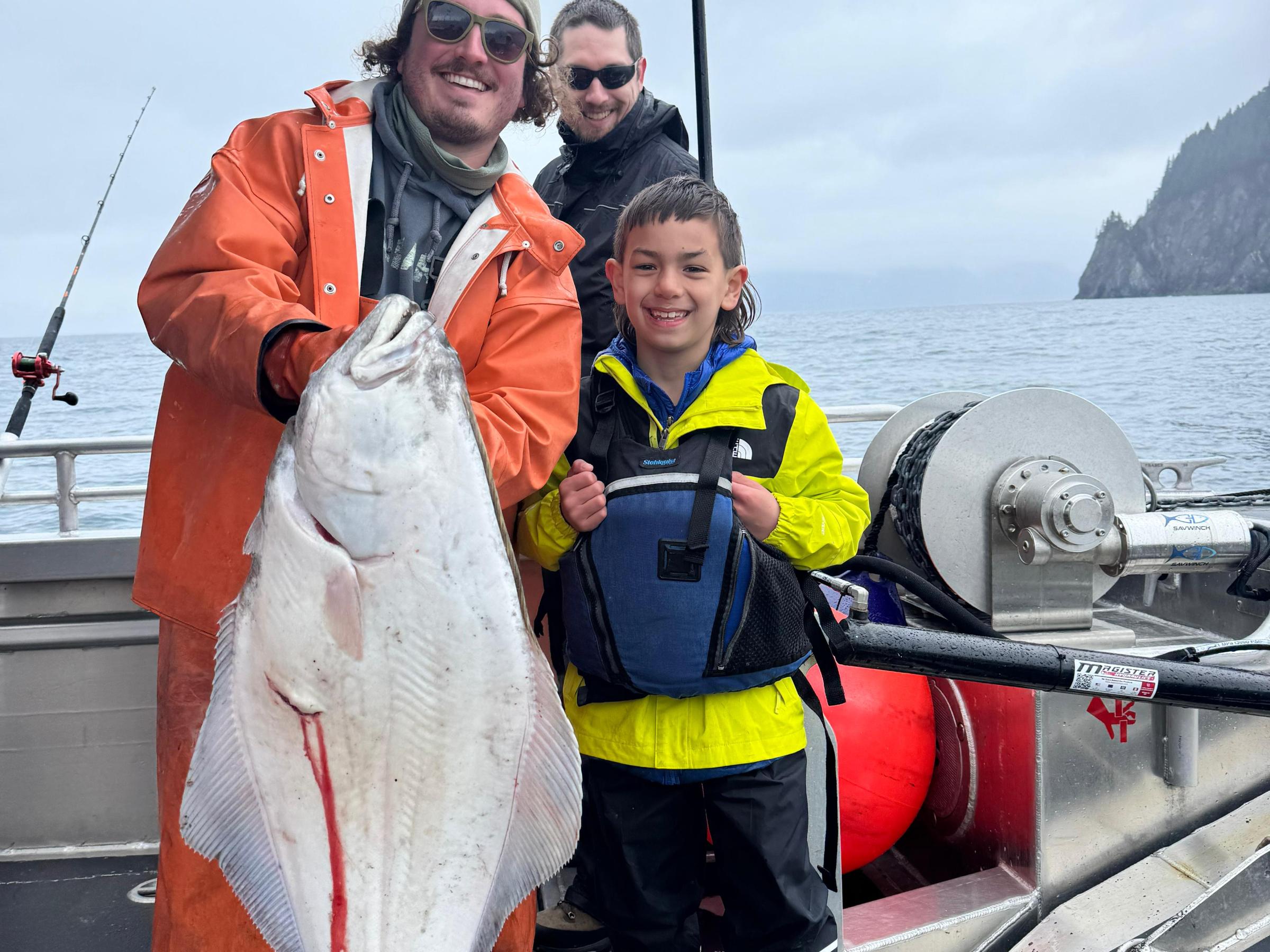 People holding a large fish on a boat; ocean and cloudy sky in background.