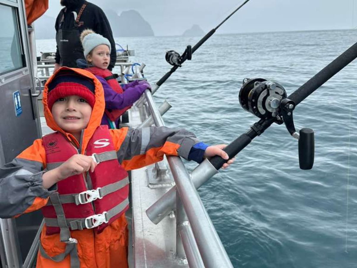 Children in rain gear fishing on a boat in overcast weather.