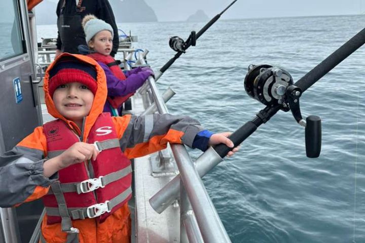 Children in rain gear fishing on a boat in overcast weather.