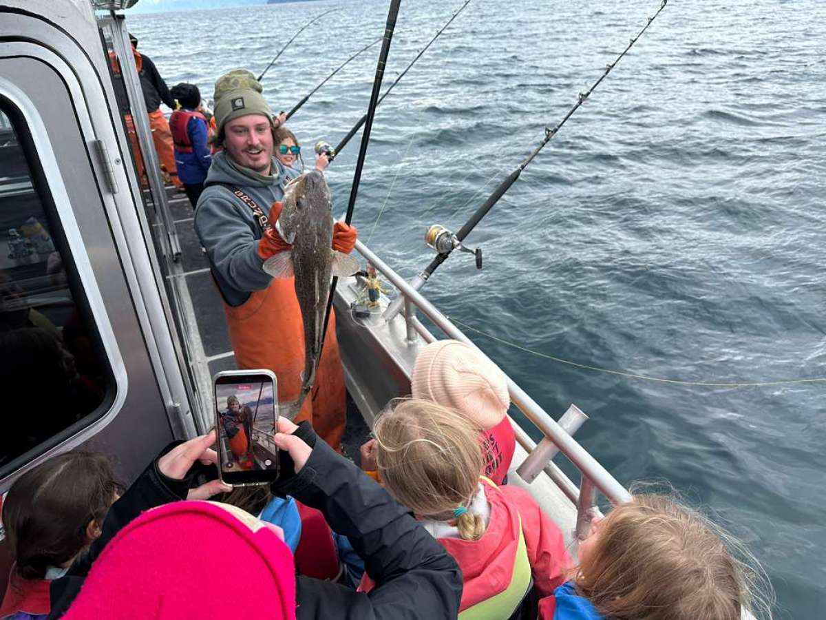 Man on boat holds a fish, surrounded by people taking photos.