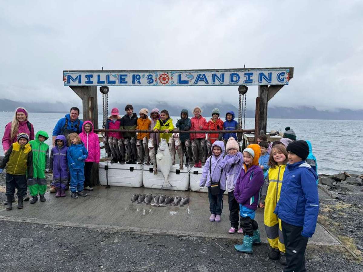 Group of kids and adults in colorful rain gear with fish at dock.