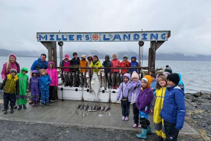 Group of kids and adults in colorful rain gear with fish at dock.