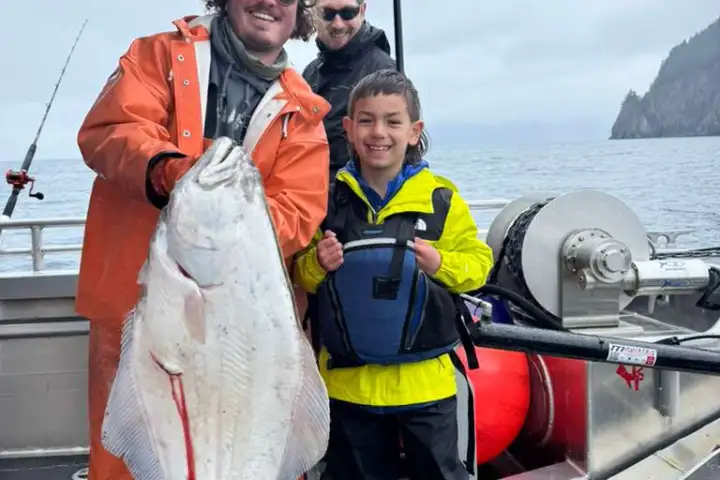 Two people on a boat holding a large fish, with cloudy skies in the background.
