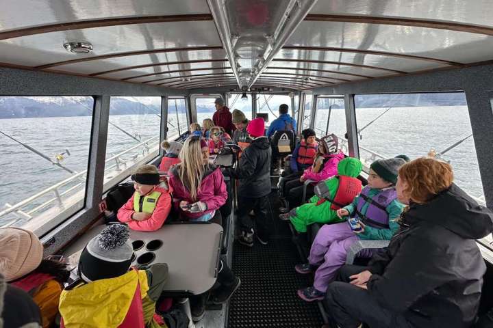 Passengers, including children, sitting inside a boat with large windows overlooking the sea.