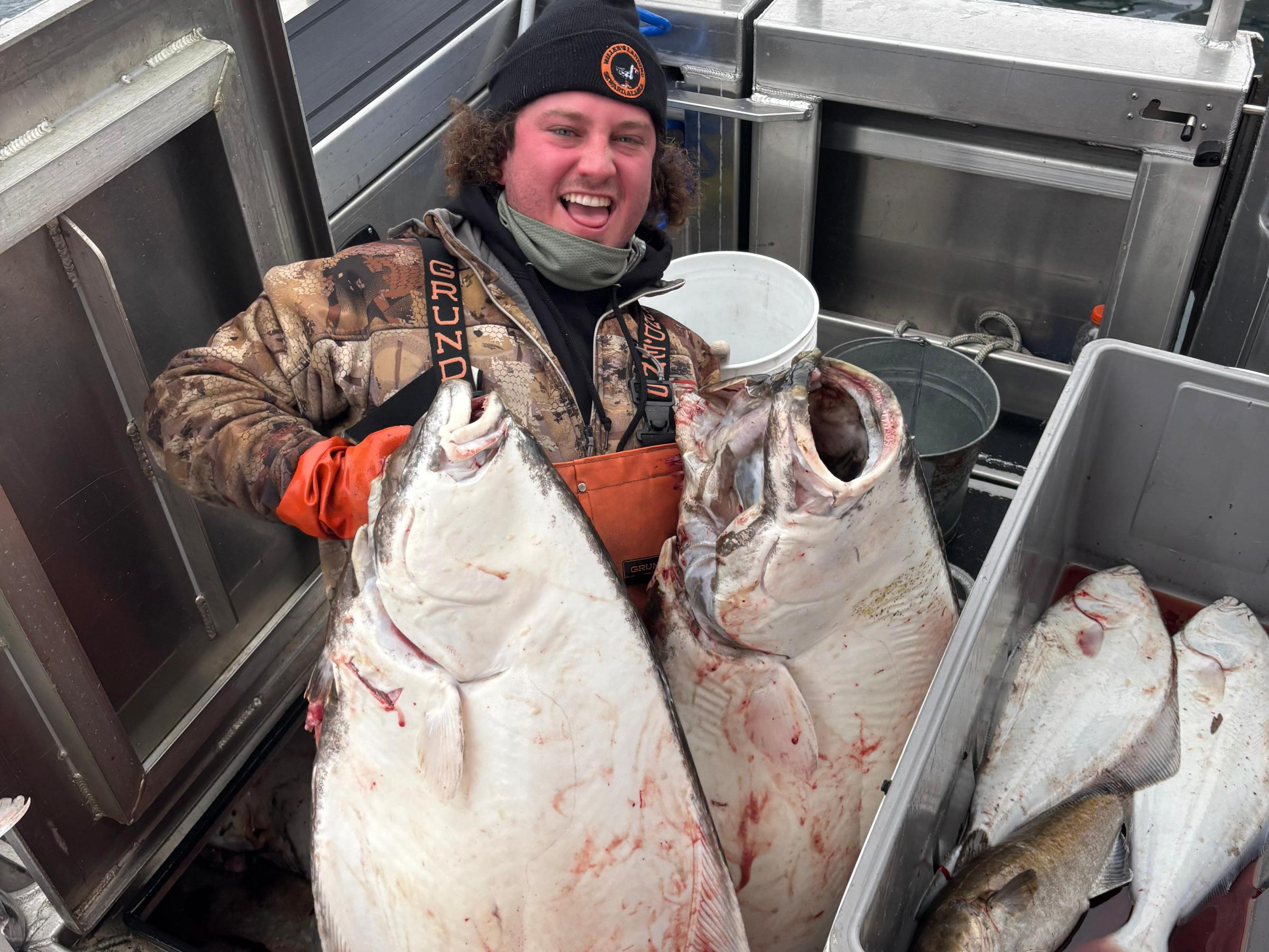 Person smiling on a boat holding large fish, surrounded by fishing equipment.