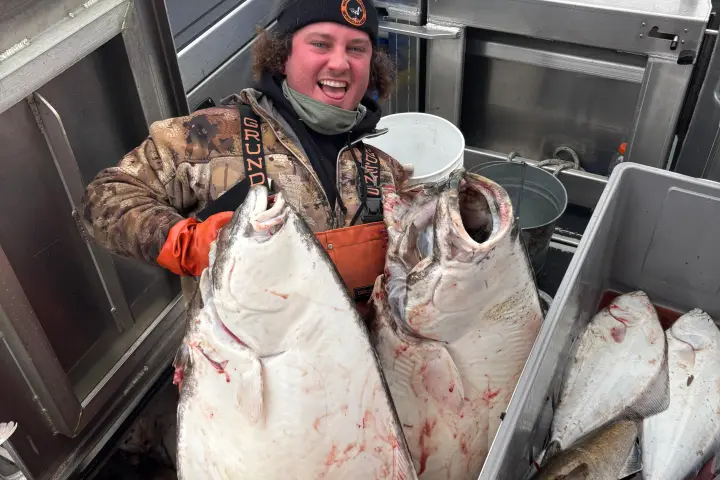 Person smiling on a boat holding large fish, surrounded by fishing equipment.