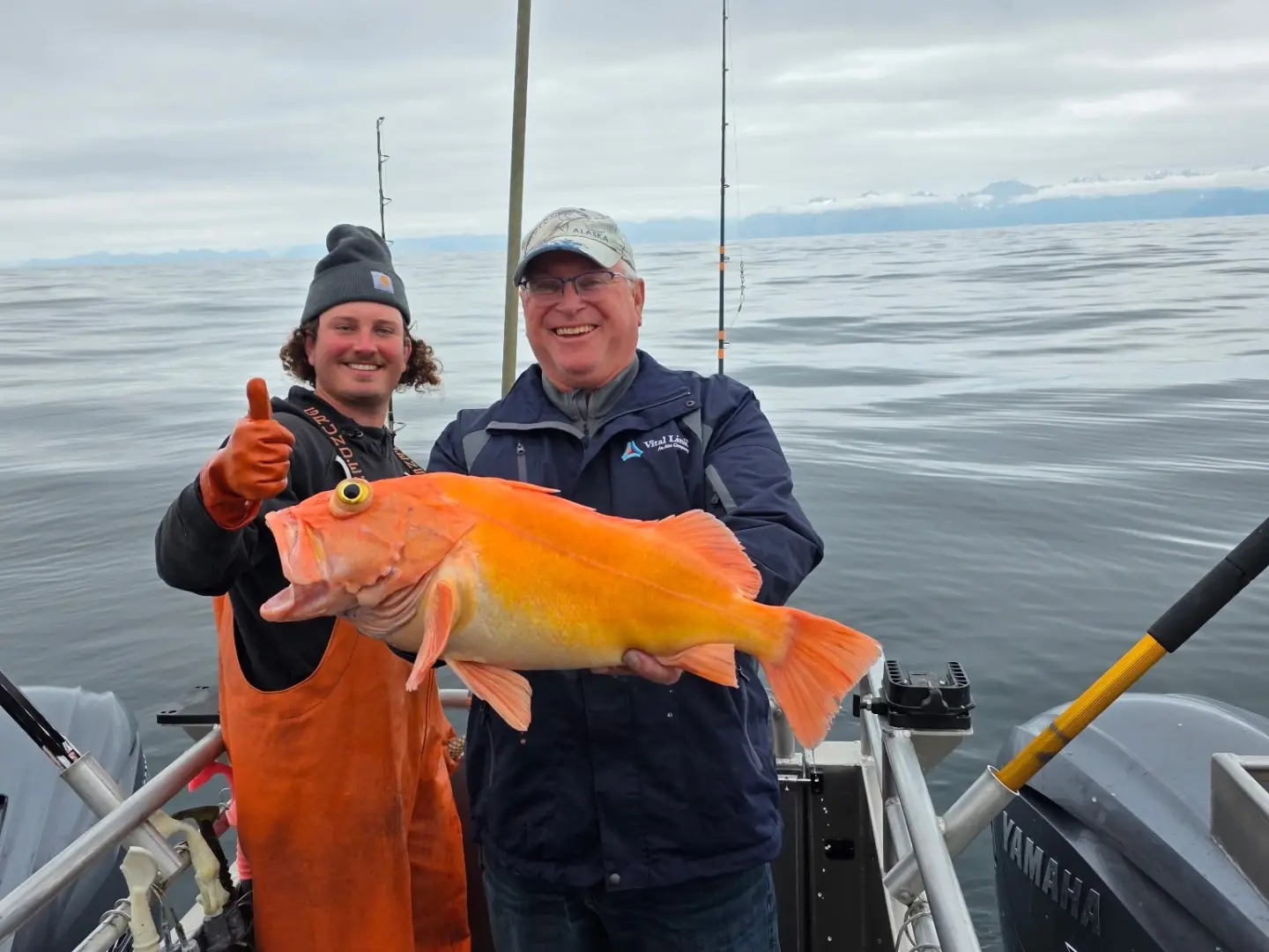 Two men on a boat holding a large fish, smiling at the camera.