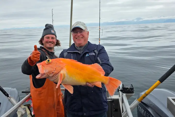Two men on a boat holding a large fish, smiling at the camera.