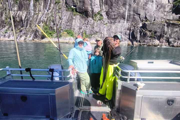 Group on boat with large fish catch, rocky cliff in background.