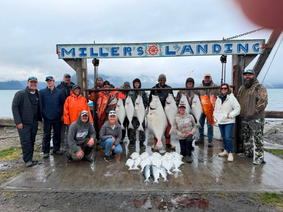 Group of people posing with caught fish under 'Miller's Landing' sign near a body of water.