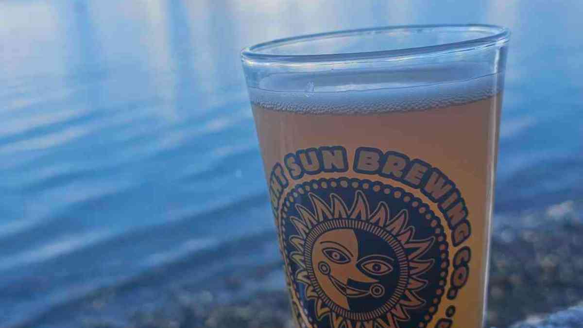 Glass of beer with logo on a wooden ledge, snowy mountains and lake in background.