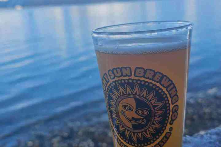 Glass of beer with logo on a wooden ledge, snowy mountains and lake in background.