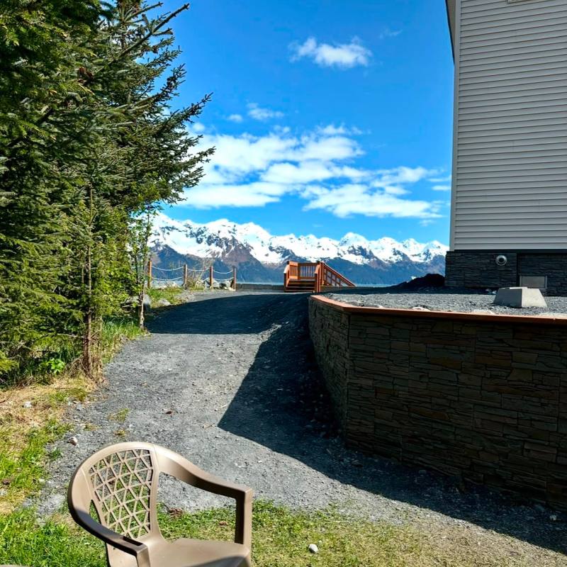 Plastic chair outside house with mountain view under blue sky.