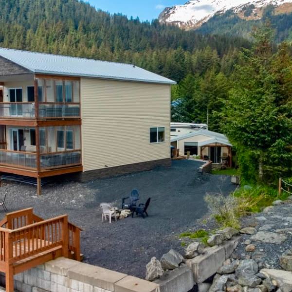 Three-story building with balconies near forested hillside and mountains.
