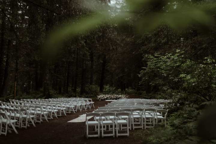 Outdoor wedding setup with white chairs in a forest setting.