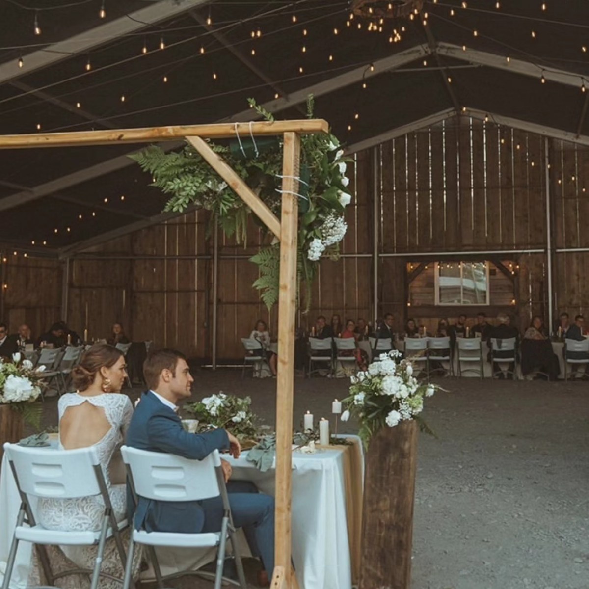 Couple seated at a table in a rustic barn wedding venue with string lights hanging.
