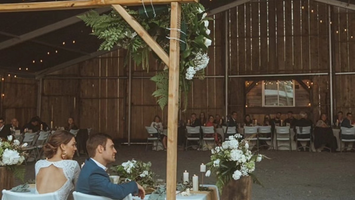 Couple seated at a table in a rustic barn wedding venue with string lights hanging.
