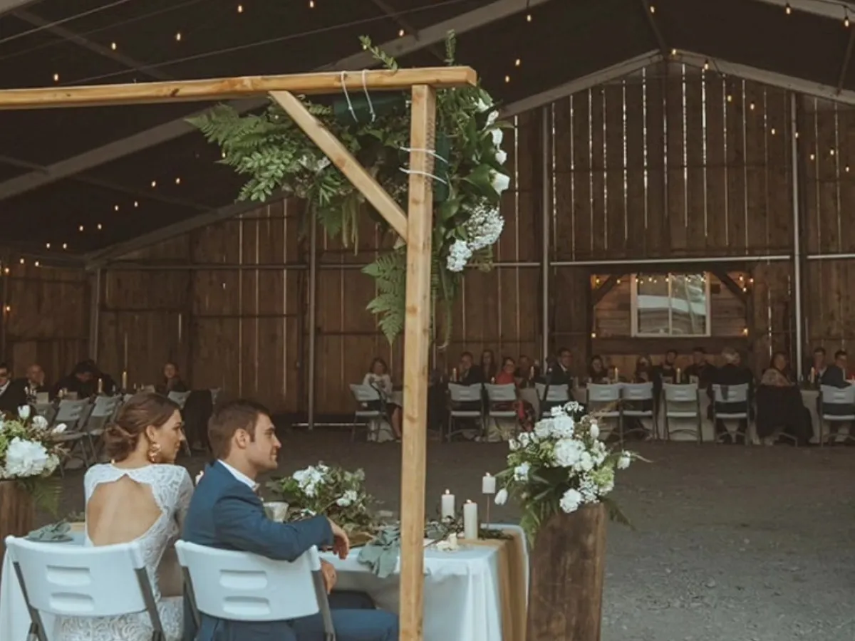 Couple seated at a table in a rustic barn wedding venue with string lights hanging.