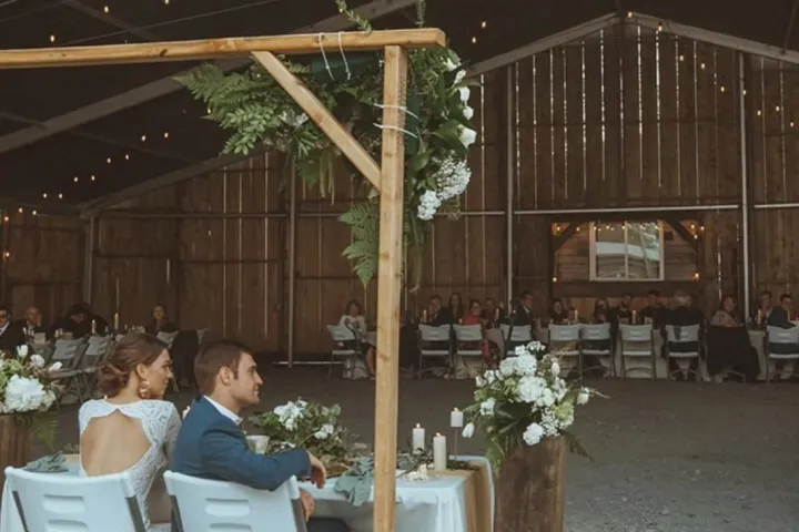 Couple seated at a table in a rustic barn wedding venue with string lights hanging.