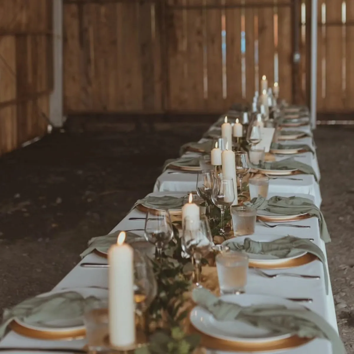 Long dining table with candles, plates, and glasses, set in a rustic wooden venue.