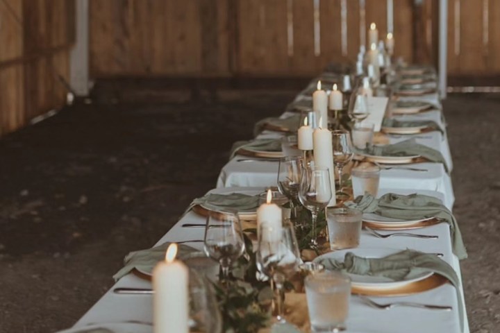 Long dining table with candles, plates, and glasses, set in a rustic wooden venue.