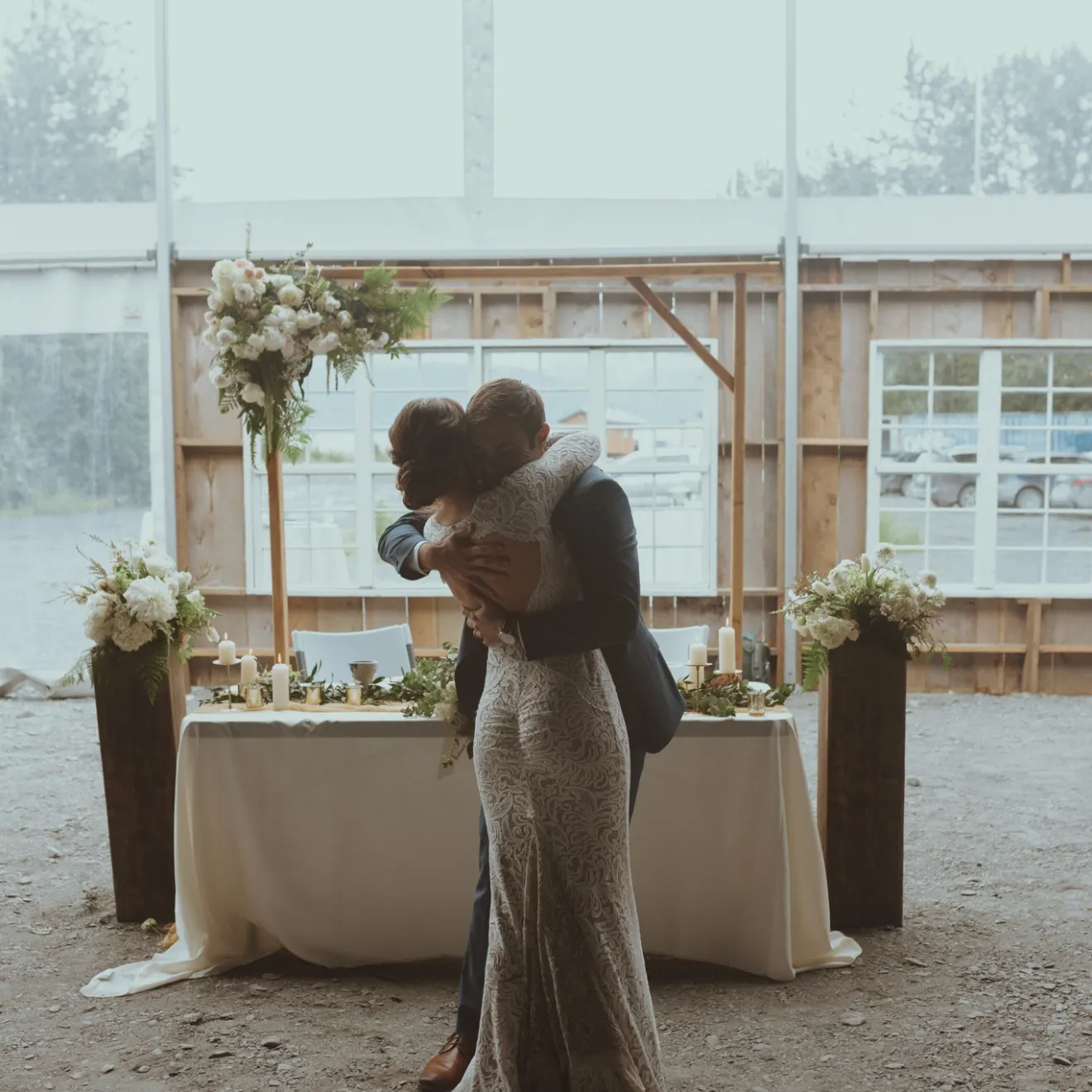 Couple hugging in front of a decorated table and flowers in a tented setting.
