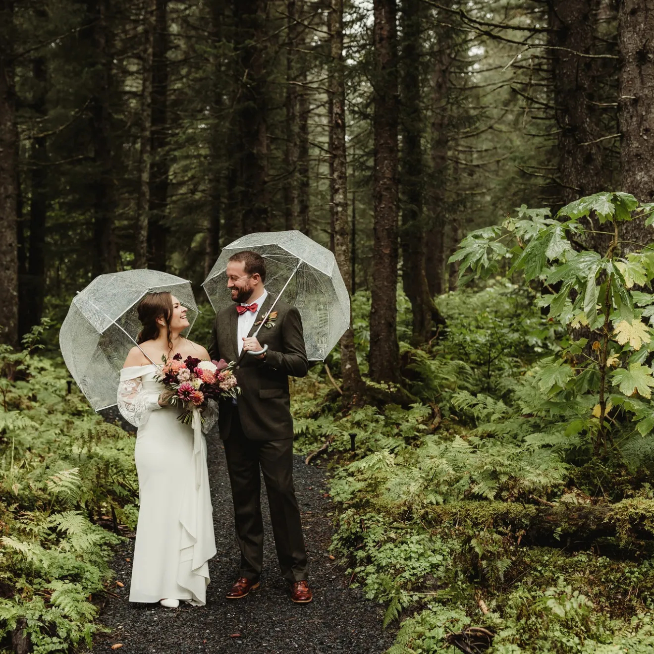 Bride and groom with umbrellas walking in a lush forest.