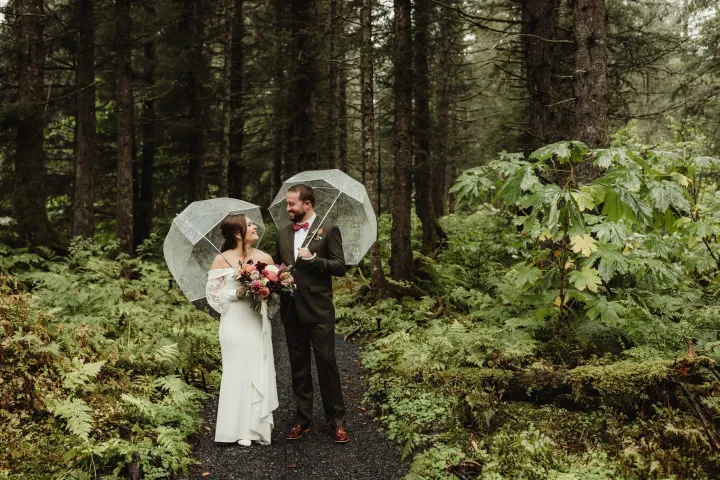 Bride and groom with umbrellas walking in a lush forest.