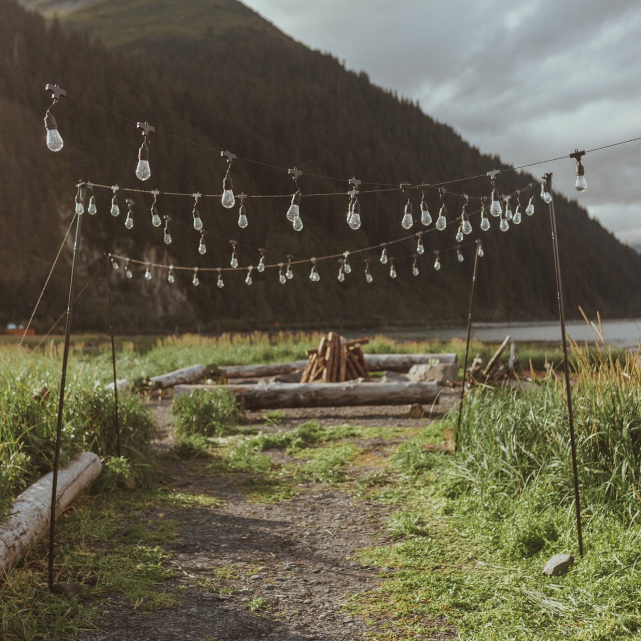 String lights hanging over a rustic outdoor path with mountains in the background.