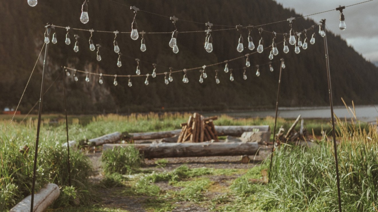 String lights hanging over a rustic outdoor path with mountains in the background.