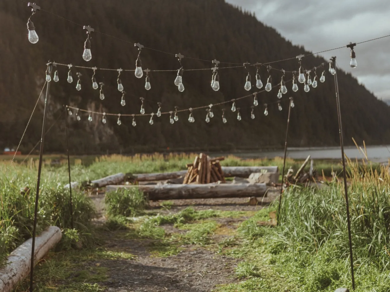 String lights hanging over a rustic outdoor path with mountains in the background.