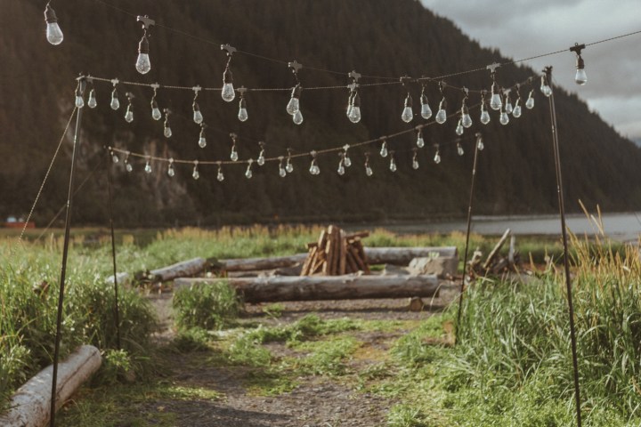 String lights hanging over a rustic outdoor path with mountains in the background.
