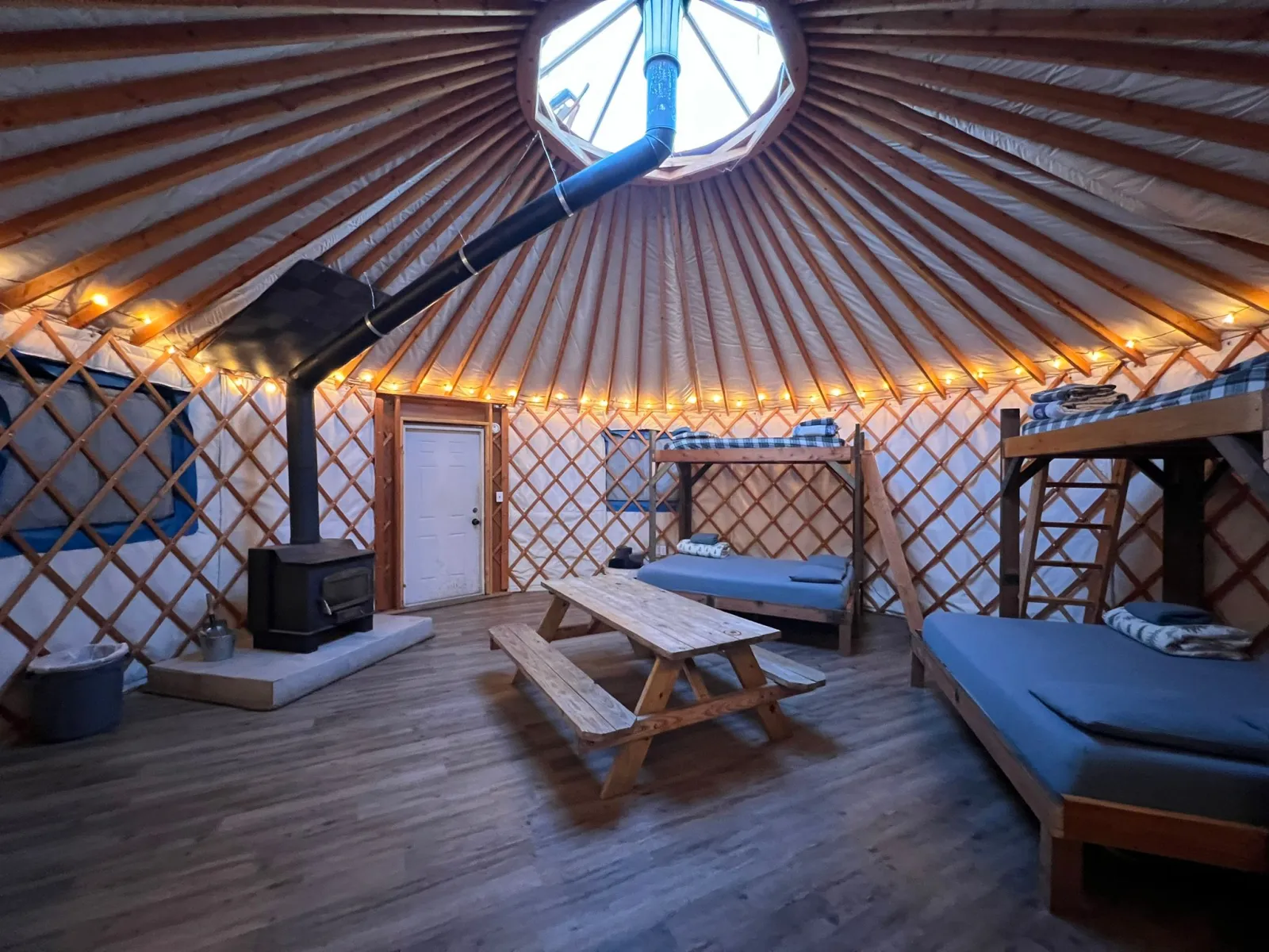 inside a Yurt with a iron stove, picnic table and 2 bunk beds