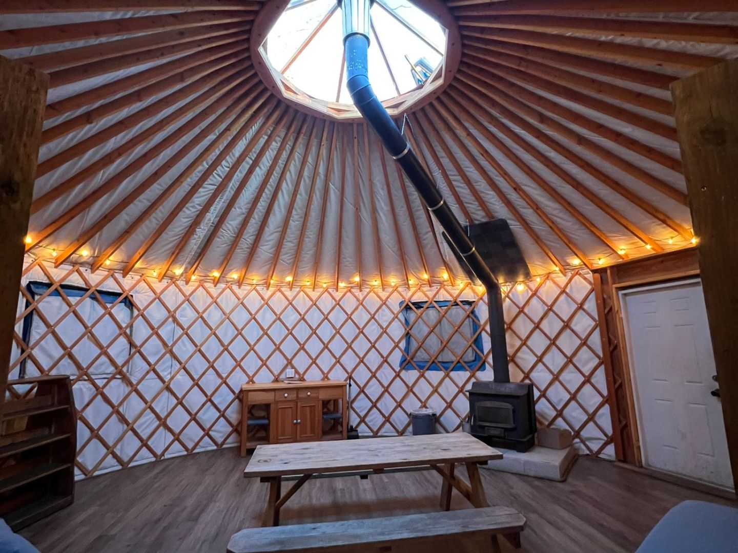 inside a Yurt with a iron stove and picnic table illuminated by led lights