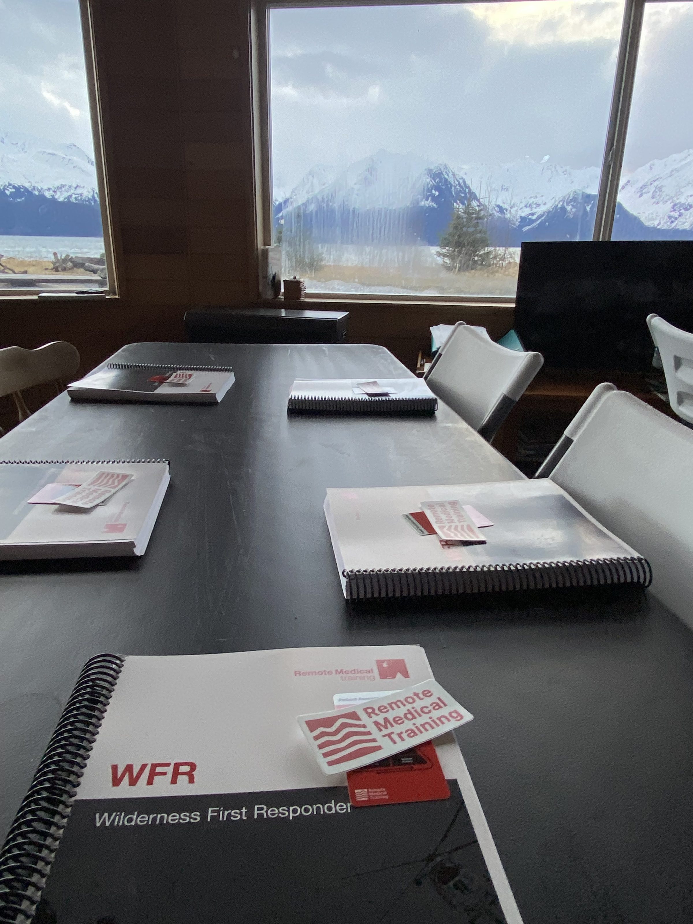 Wilderness First Responder booklets on a table, snowy mountains visible through windows.