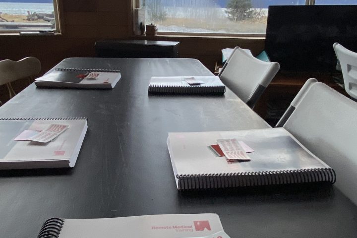 Wilderness First Responder booklets on a table, snowy mountains visible through windows.