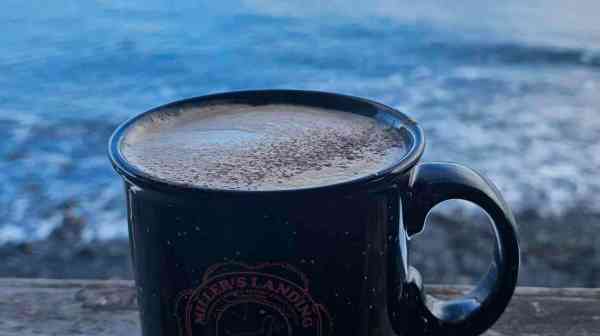 a cup of coffee sitting next to a body of water