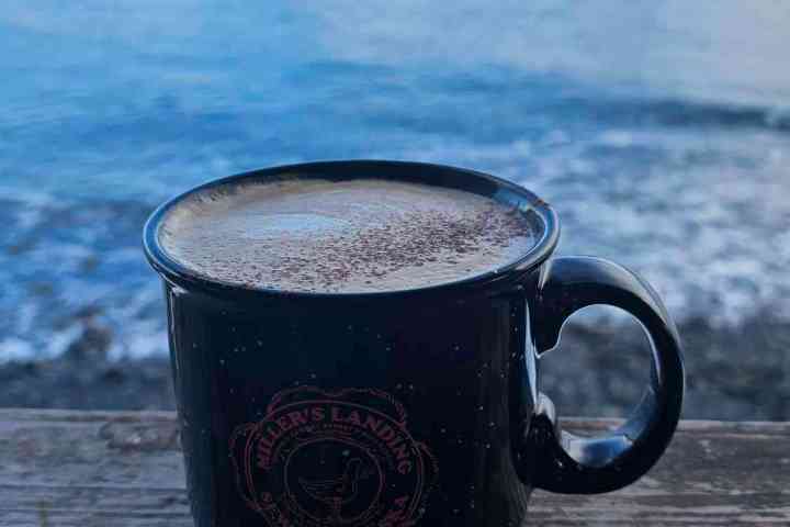 a cup of coffee sitting next to a body of water