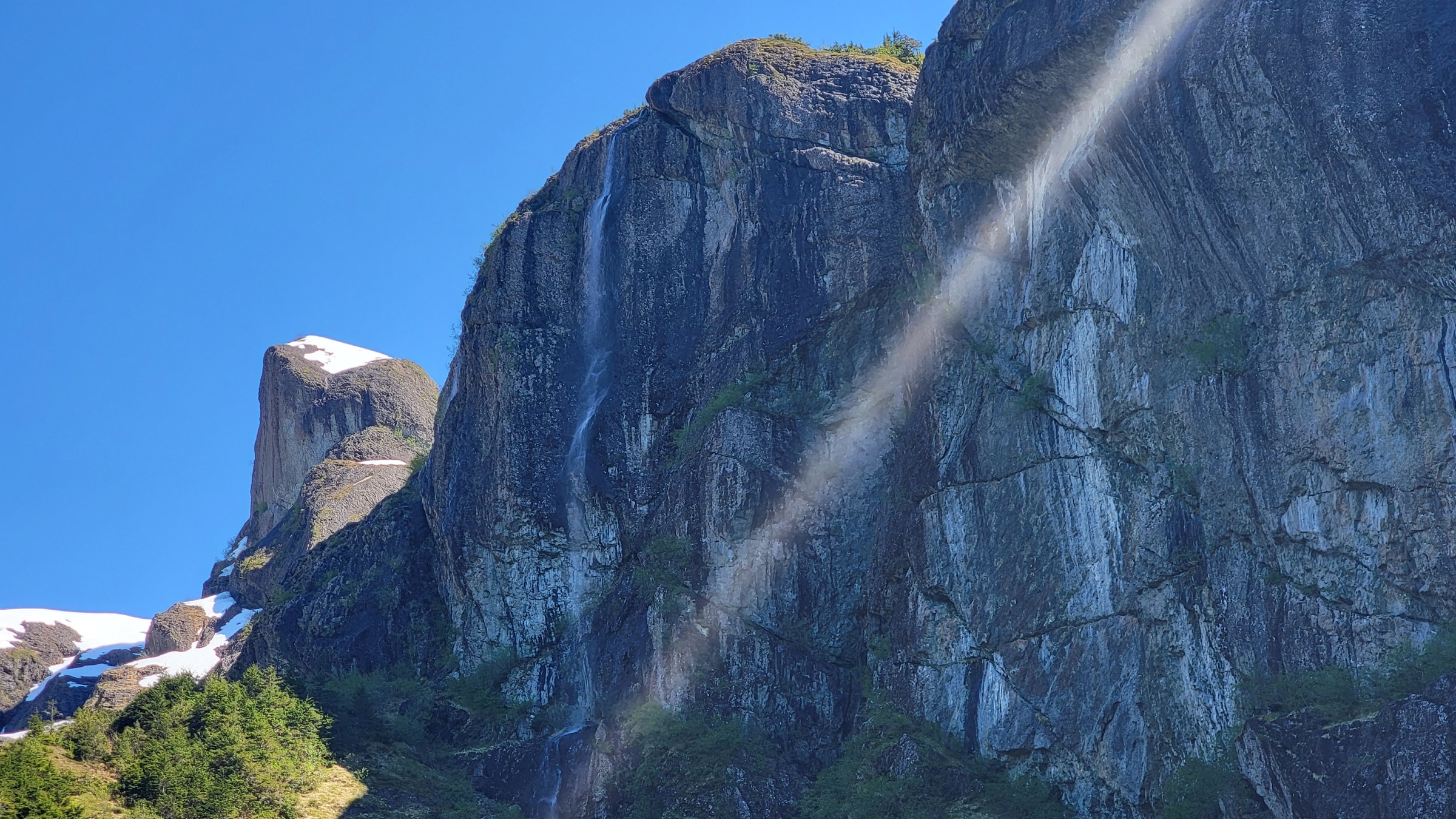 a waterfall with trees on the side of a mountain