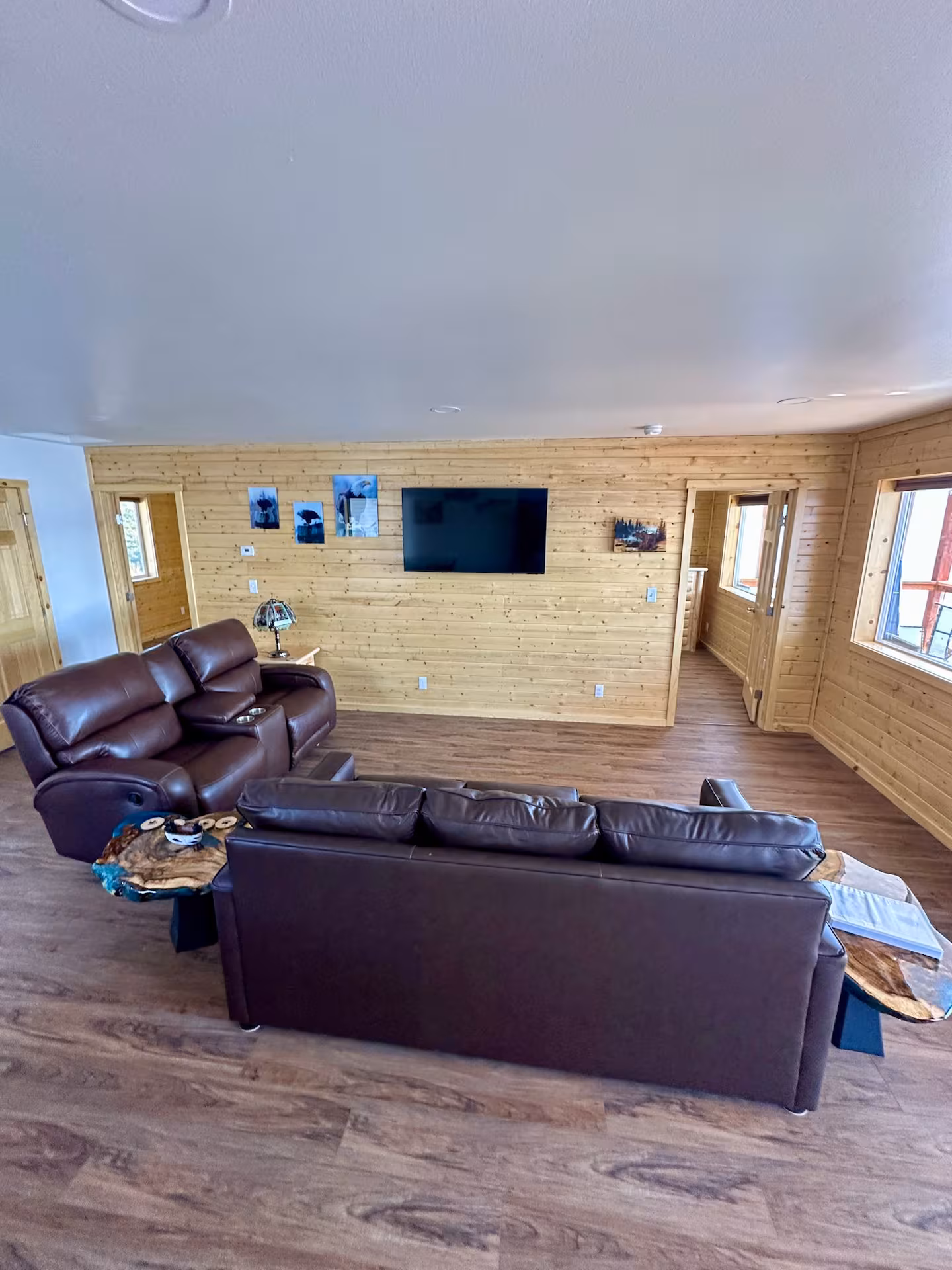 Cozy living room with brown leather sofas and wall-mounted TV on wood-paneled walls.