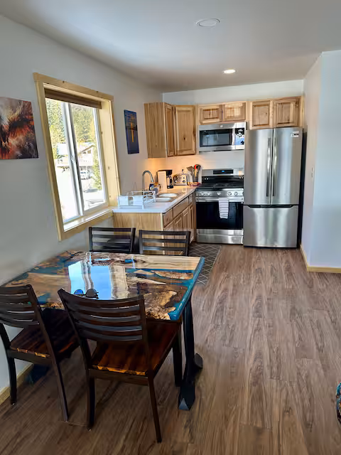 Modern kitchen with wooden cabinets, stainless steel appliances, and a wooden dining table with chairs.