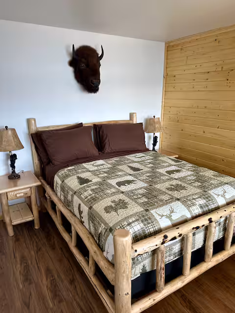 Rustic bedroom with log bed, plaid bedding, wood walls, and buffalo head on the wall.