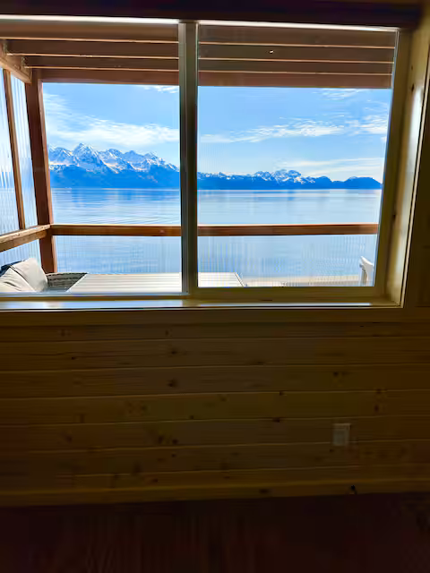 View of snowy mountains and lake through a wooden cabin window.