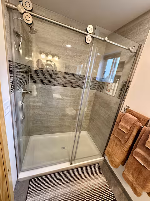 Modern glass shower with gray tiles and brown towels on a rack.
