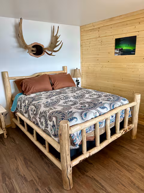Rustic bedroom with log bed, antler wall decor, paisley bedding, and wood-paneled walls.
