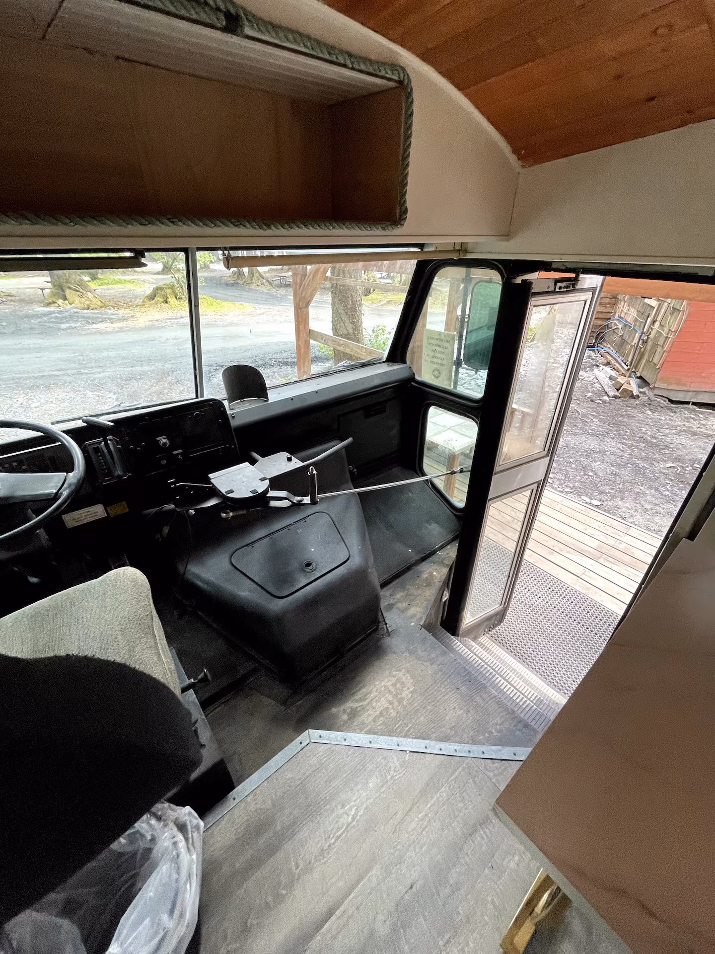 Interior of a bus with steering wheel, open door, and wooden floor.