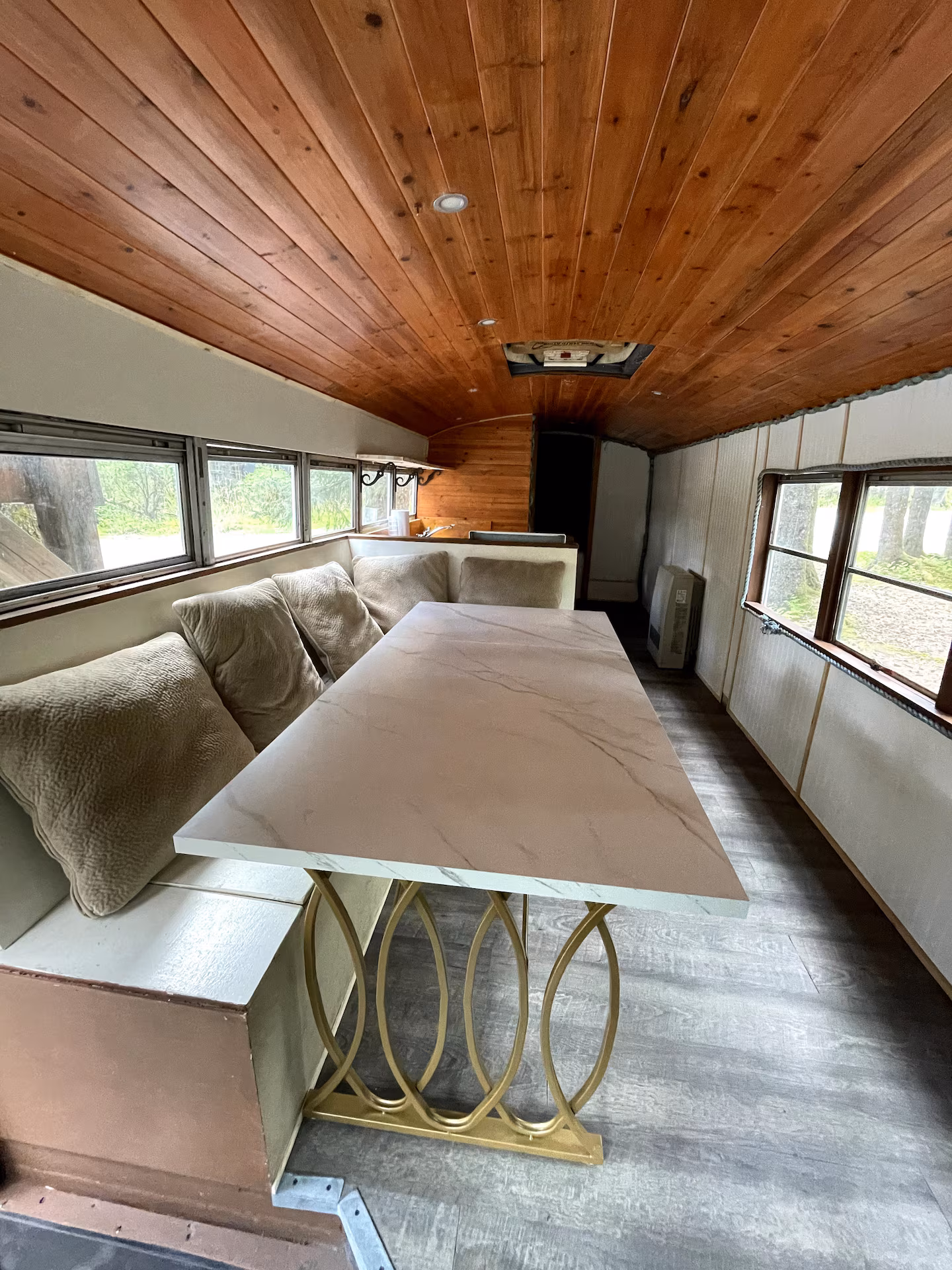 Cozy bus interior with wooden ceiling, cushioned seats, and a marble table.