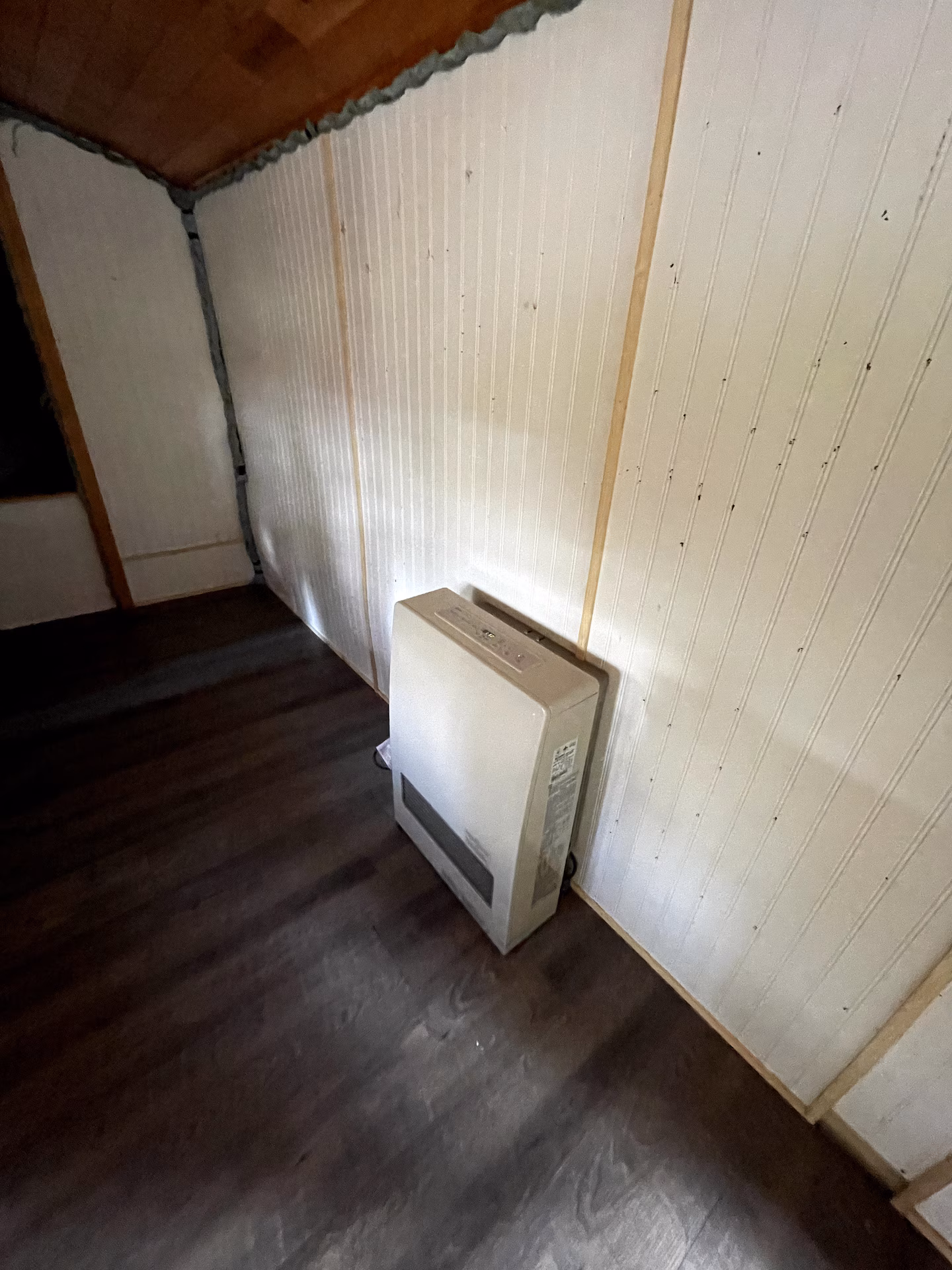 Wall-mounted heater in a corner with wood-paneled walls and ceiling.