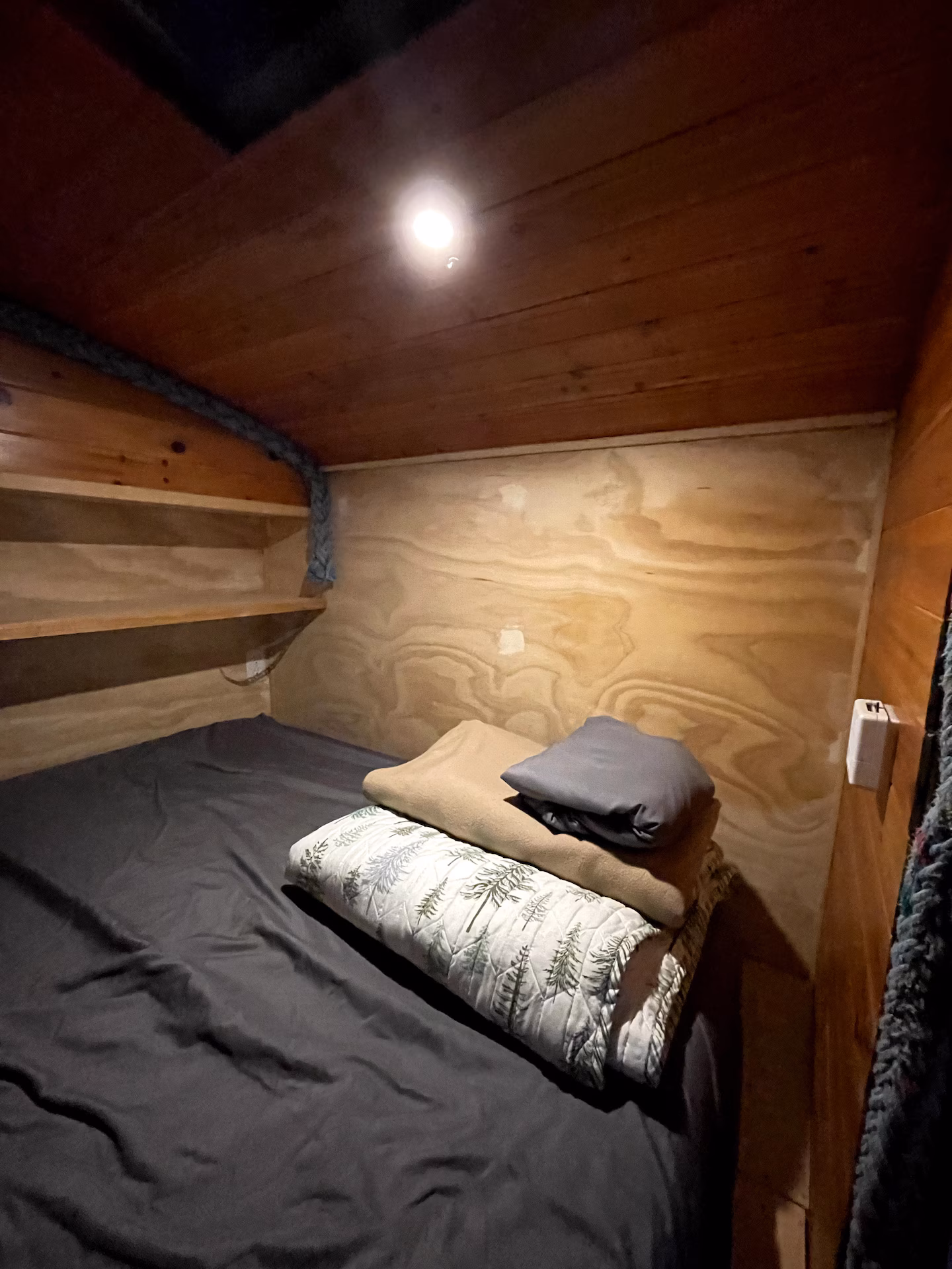 Small wooden room with a bed, blankets, and shelves.